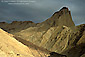Sunlight on barren hills below storm clouds and Zabriskie Point, Golden Canyon, Death Valley National Park, California
